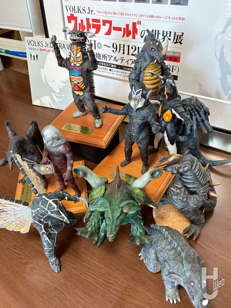 コモリプロジェクトウルトラワールドの世界展ポスター発表をバックにガレージキットが並ぶ