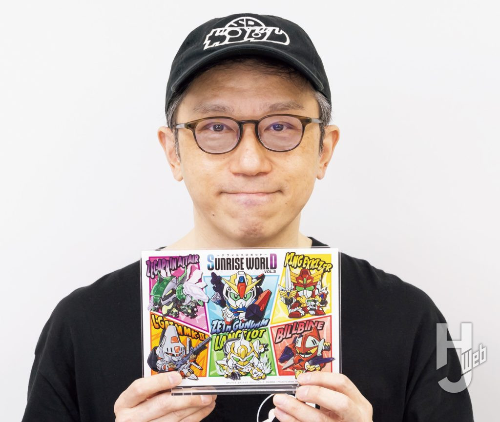 「SUNRISE WORLD ～デフォルメロボットフェア～ VOL.2」描き下ろしイラストが集合した「キービジュアルアクリルプレート」を持つ横井画伯